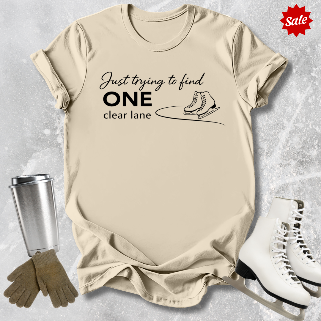 Beige  t-shirt with humorous text design, surrounded by ice skates, gloves, and a tumbler on a textured surface.