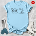 Light blue  t-shirt with humorous text design, surrounded by ice skates, gloves, and a tumbler on a textured surface.