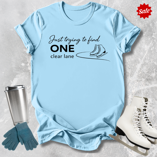 Light blue  t-shirt with humorous text design, surrounded by ice skates, gloves, and a tumbler on a textured surface.