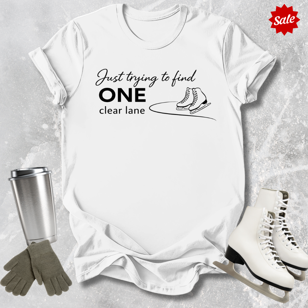 White  t-shirt with humorous text design, surrounded by ice skates, gloves, and a tumbler on a textured surface.