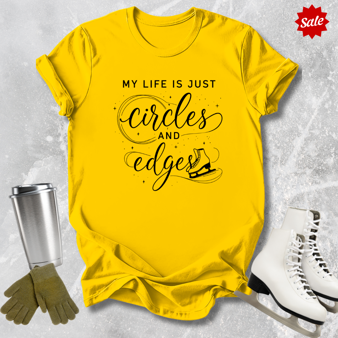 Yellow t-shirt with My Life is just circles and edges Figure Skating text, silver tumbler, green gloves, and white skates on a textured gray background.