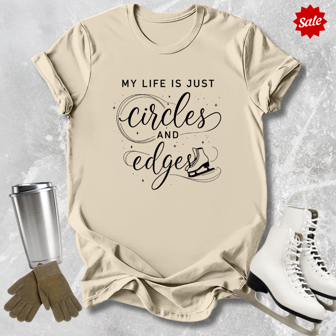 Beige t-shirt with My Life is just circles and edges Figure Skating text, silver tumbler, brown gloves, and white skates on a textured surface.