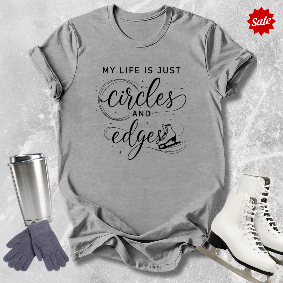 Gray t-shirt with My Life is just circles and edges Figure Skating text, silver tumbler, gray gloves, and white skates on a textured surface.