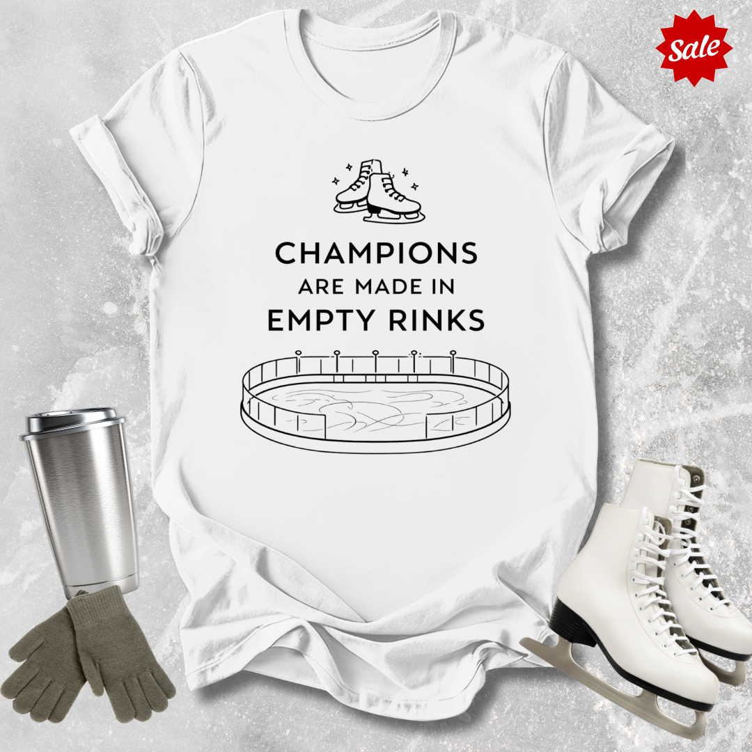 White t-shirt with a figure skating design and Champions are Made in Empty Rinks text, surrounded by ice skates and a tumbler on a textured surface.