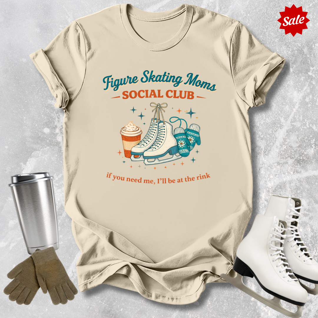Beige t-shirt with figure skating graphic and text, surrounded by ice skates, gloves, and a tumbler on a textured surface.