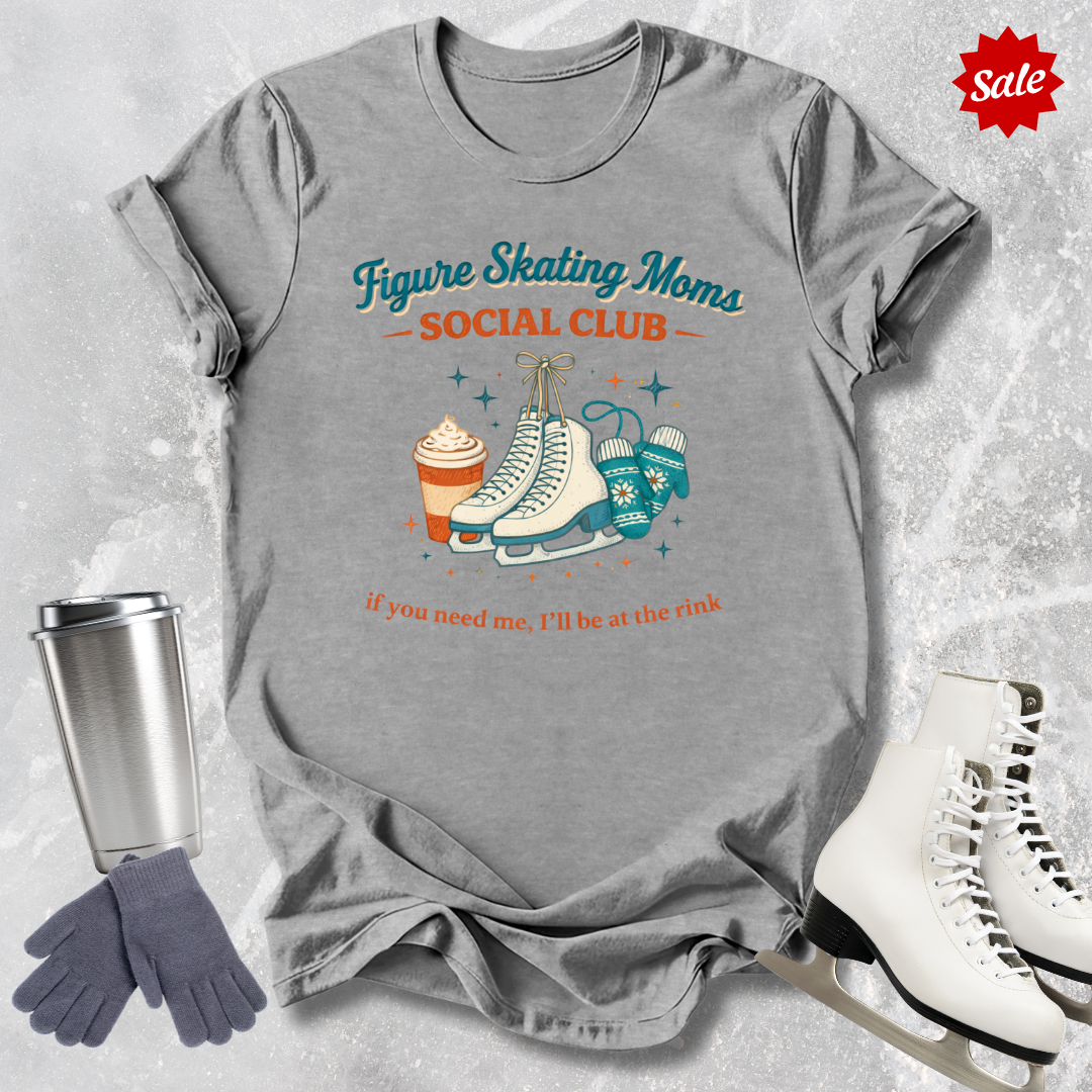 Gray t-shirt with figure skating-themed design, surrounded by ice skates, gloves, and a travel mug on a textured surface.
