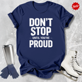 Navy blue t-shirt with 'Don't Stop Until You're Proud' text, next to a silver tumbler, gloves, and white skates on a textured gray background.