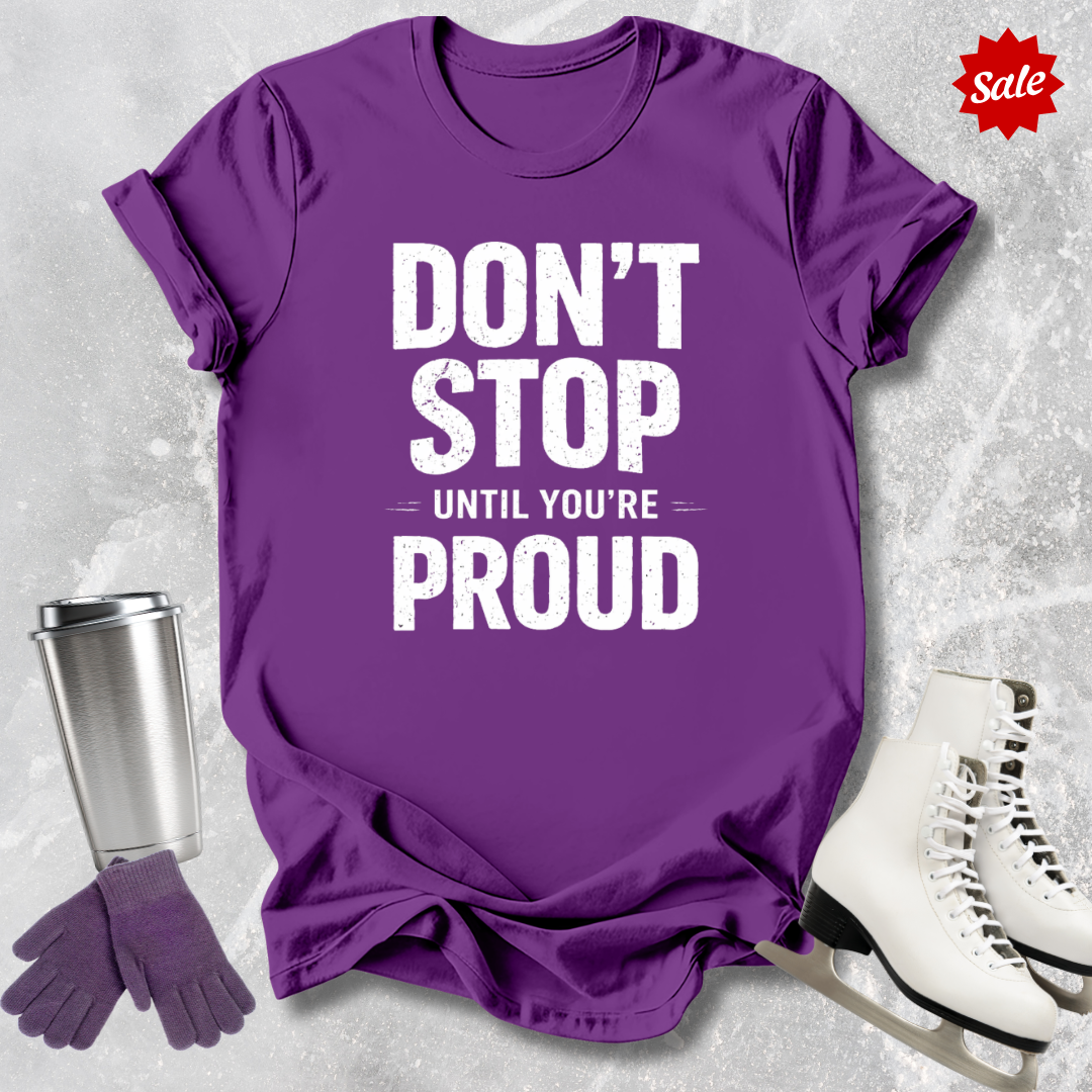 Purple t-shirt with 'Don't Stop Until You're Proud' text, next to a silver tumbler and white skates on a light gray background.