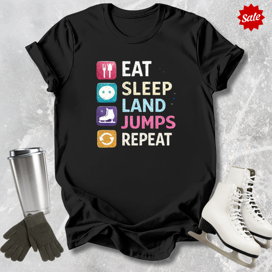 Black t-shirt with colorful graphic and text 'Eat Sleep Land Jumps Repeat' on a textured surface with ice skates and a tumbler.