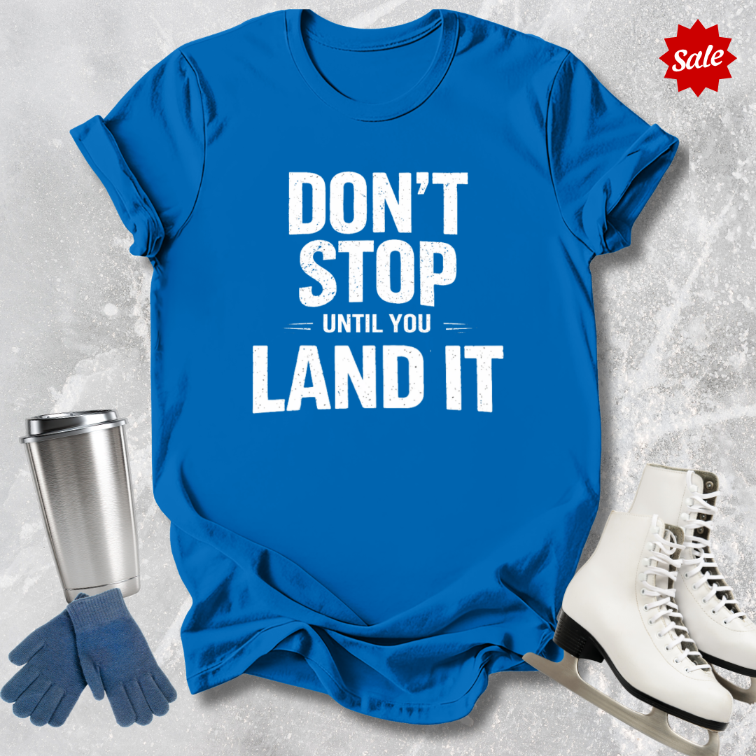 Blue t-shirt with motivational quote, silver tumbler, blue gloves, and white skates on a textured surface.
