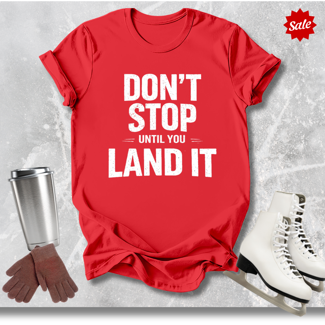 Red t-shirt with motivational quote, next to a cup, gloves, and skates on a textured gray background.
