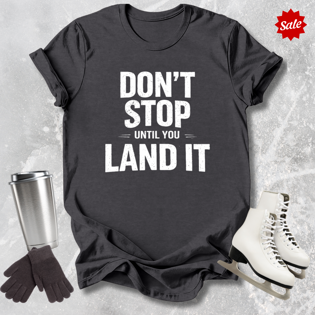 Black t-shirt with motivational quote, surrounded by a travel mug, gloves, and skates on a textured surface.