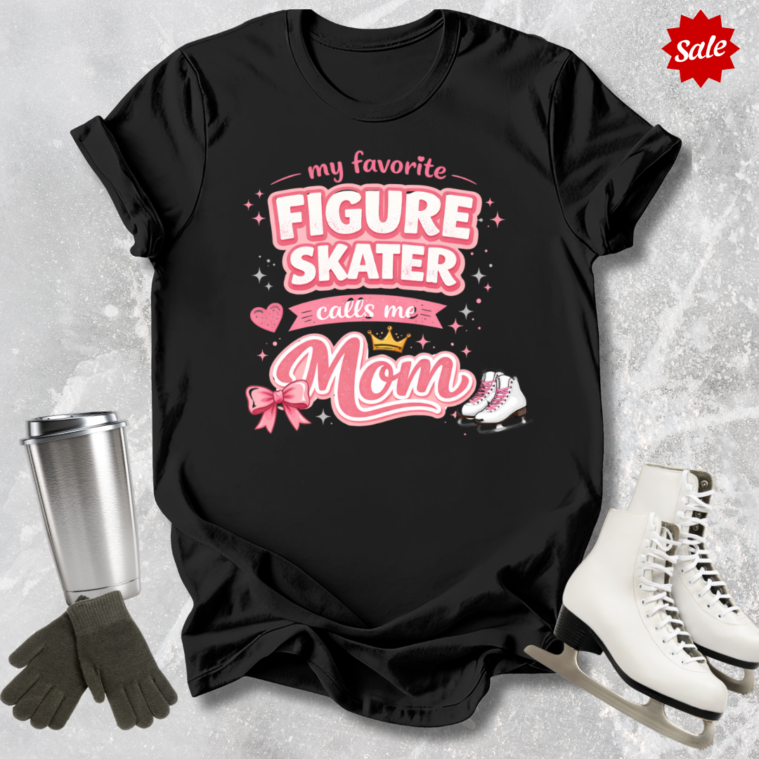 Black t-shirt with pink text 'my favorite figure skater calls me Mom' on a textured gray background with ice skates and gloves.