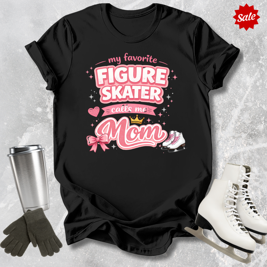 Black t-shirt with pink text 'my favorite figure skater calls me Mom' on a textured gray background with ice skates and gloves.