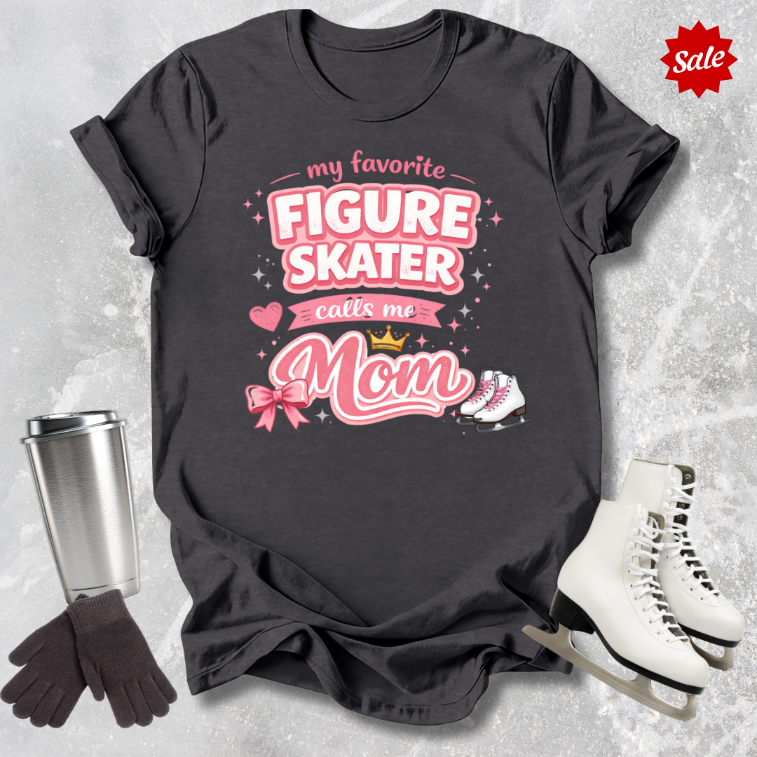 Black t-shirt with pink text 'My favorite figure skater calls me Mom' on a textured gray background.