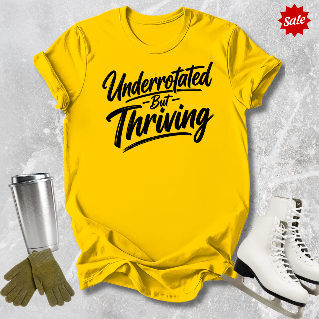 Yellow t-shirt with 'Underrotated But Thriving' text, surrounded by a silver tumbler, green gloves, and white skates on a textured gray background.