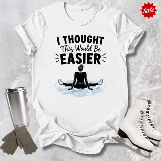 White t-shirt with 'I Thought This Would Be Easier' graphic, surrounded by ice skates, gloves, and a tumbler on a textured surface.