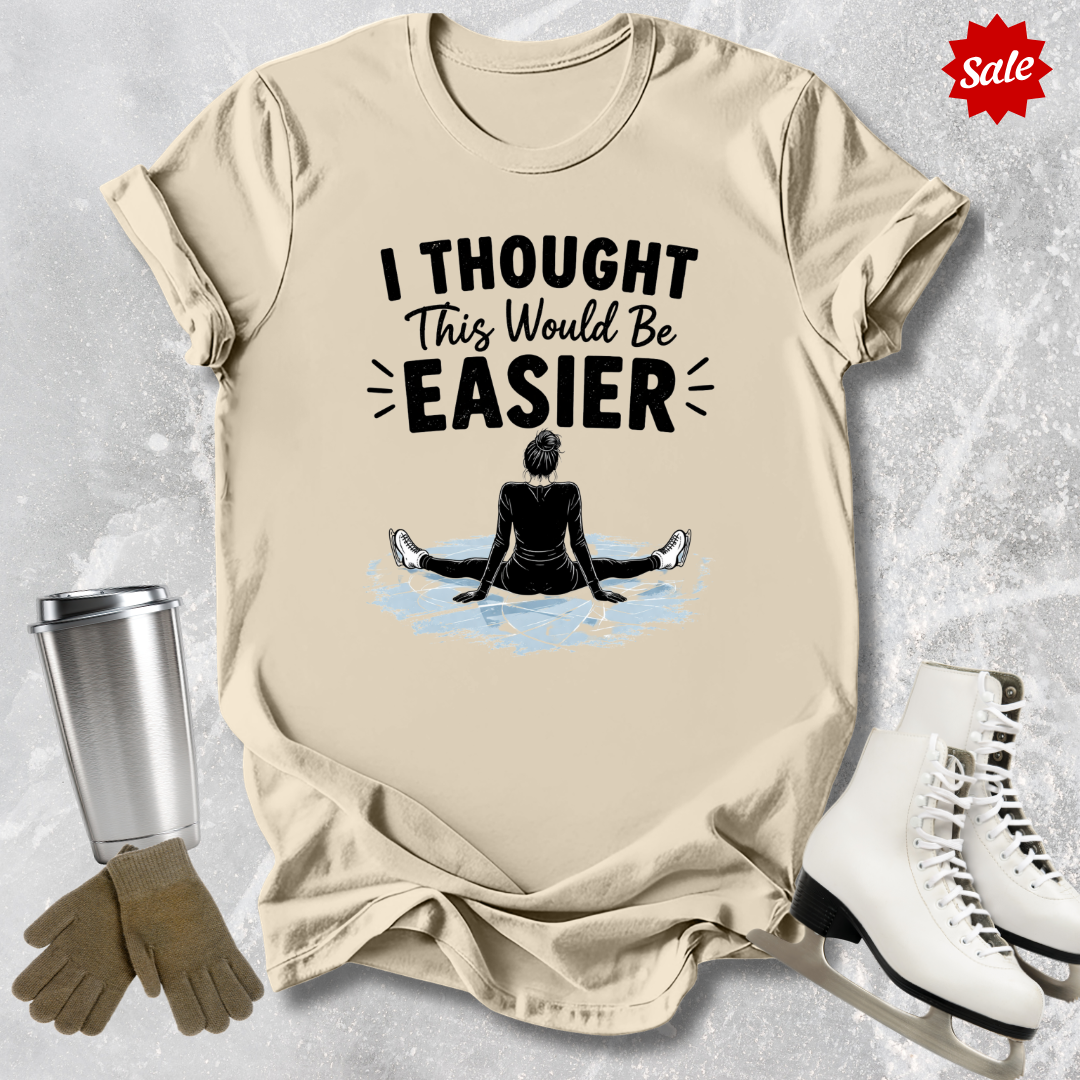Beige t-shirt with 'I Thought This Would Be Easier' graphic and accessories on a textured surface.