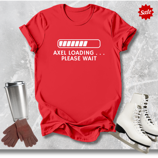 Red t-shirt with ' Axel Loading Please Wait' text, next to a silver tumbler, brown gloves, and white skates on a light gray background.