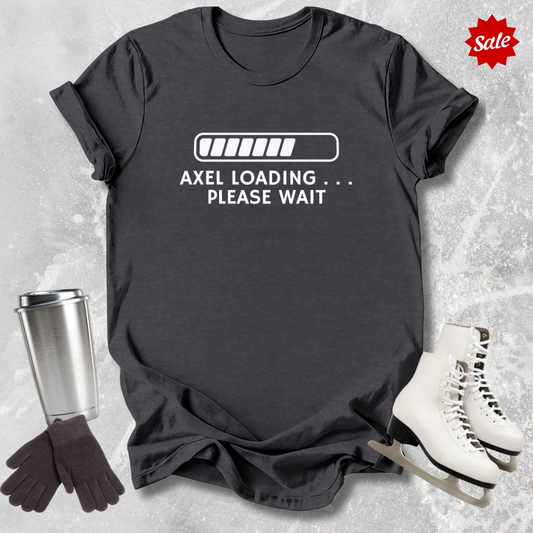 Black t-shirt with 'Axel Loading Please Wait' text, next to a silver tumbler, gloves, and white skates on a textured gray background.
