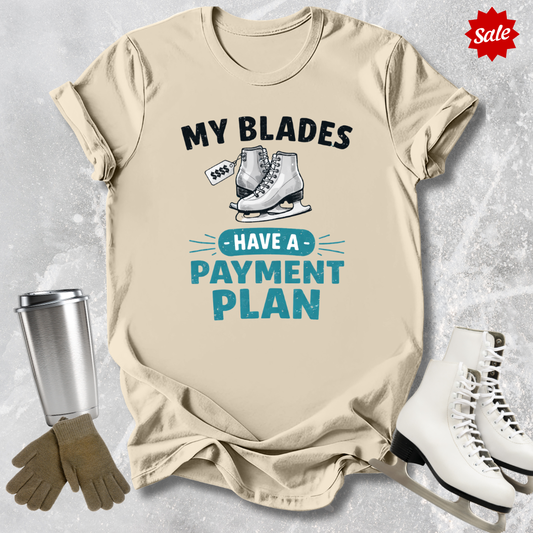 Beige t-shirt with ice skating graphic and text, surrounded by ice skates and a tumbler on a textured surface.