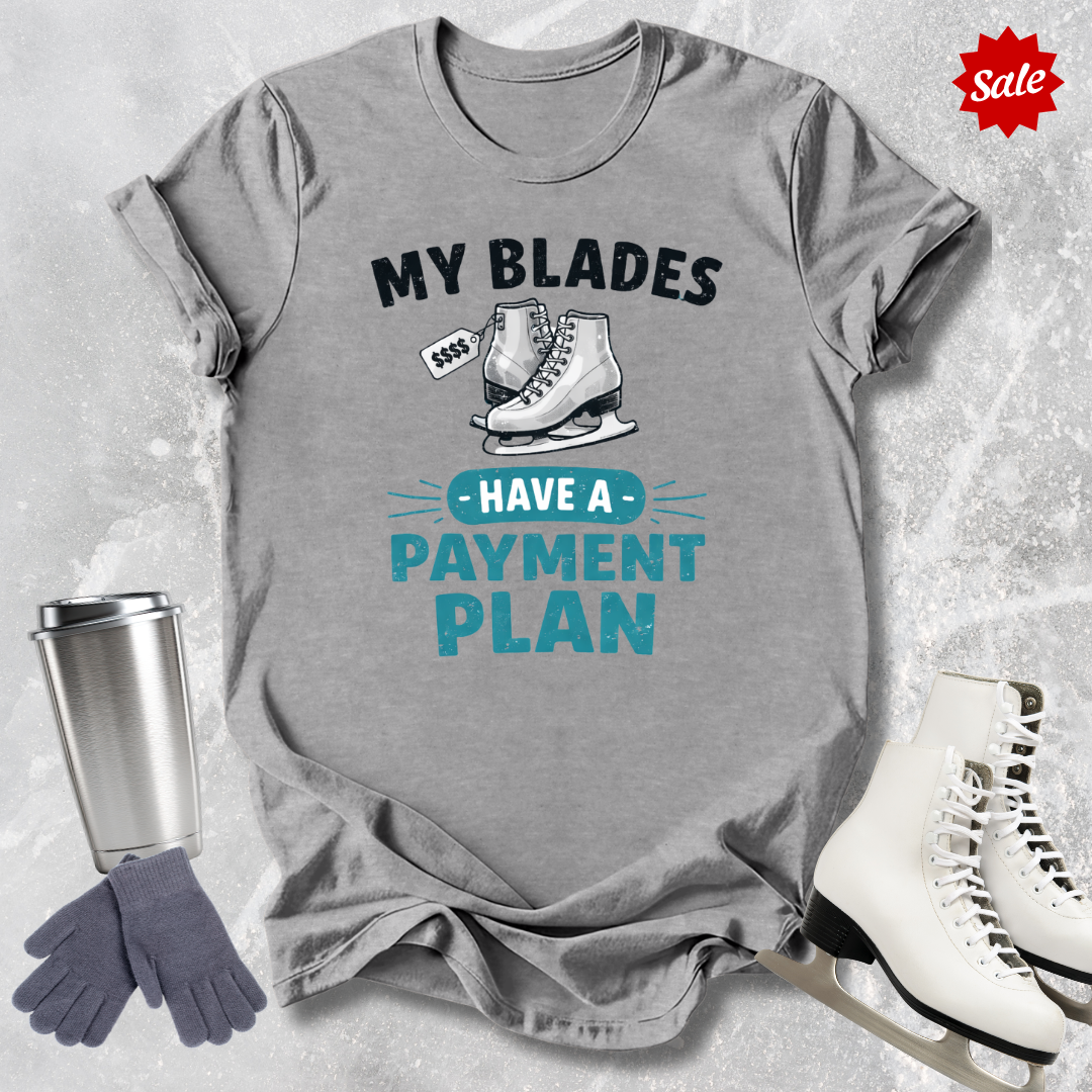 Gray t-shirt with humorous ice skating graphic and text, surrounded by ice skates and a tumbler on a textured gray background.