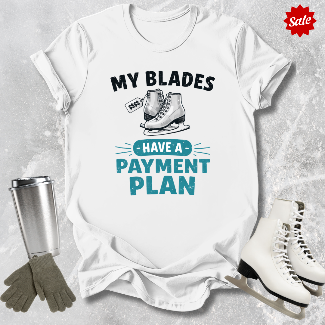 White t-shirt with ice skating graphic and text, surrounded by ice skates and a tumbler on a textured surface.