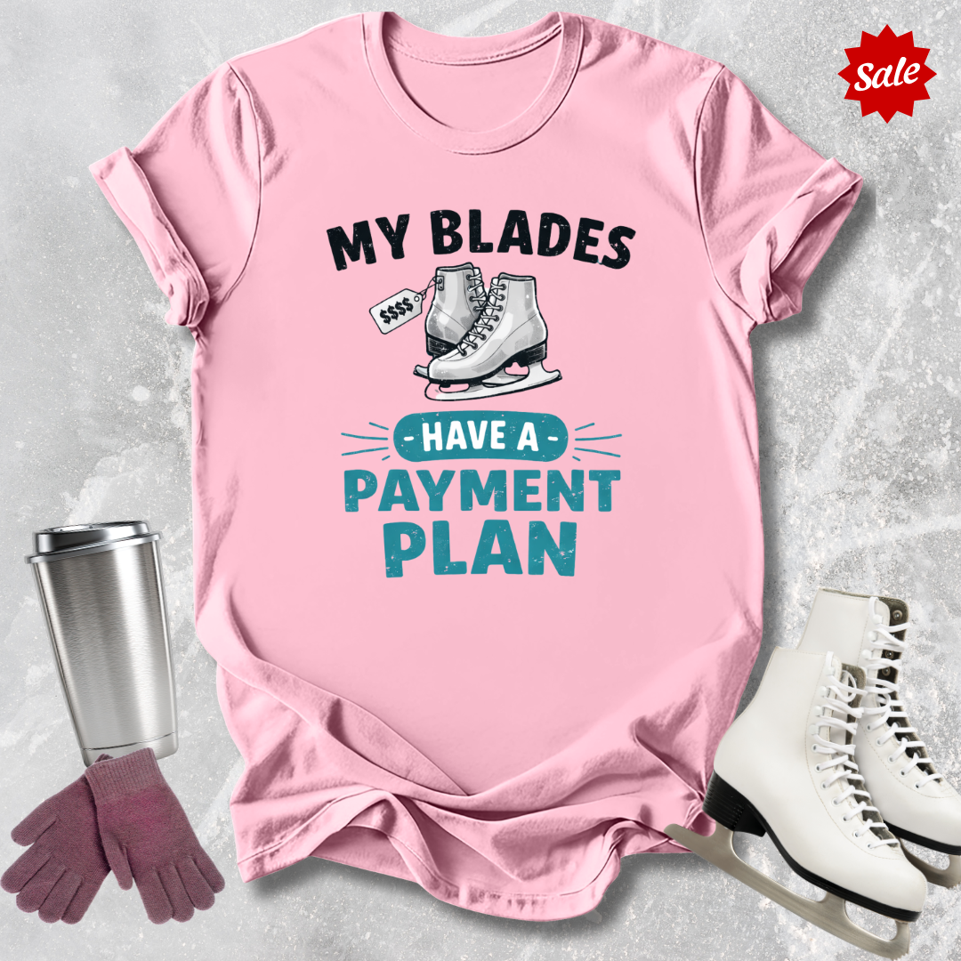 Pink t-shirt with humorous ice skating graphic and text, surrounded by ice skates, gloves, and a tumbler on a light gray background.