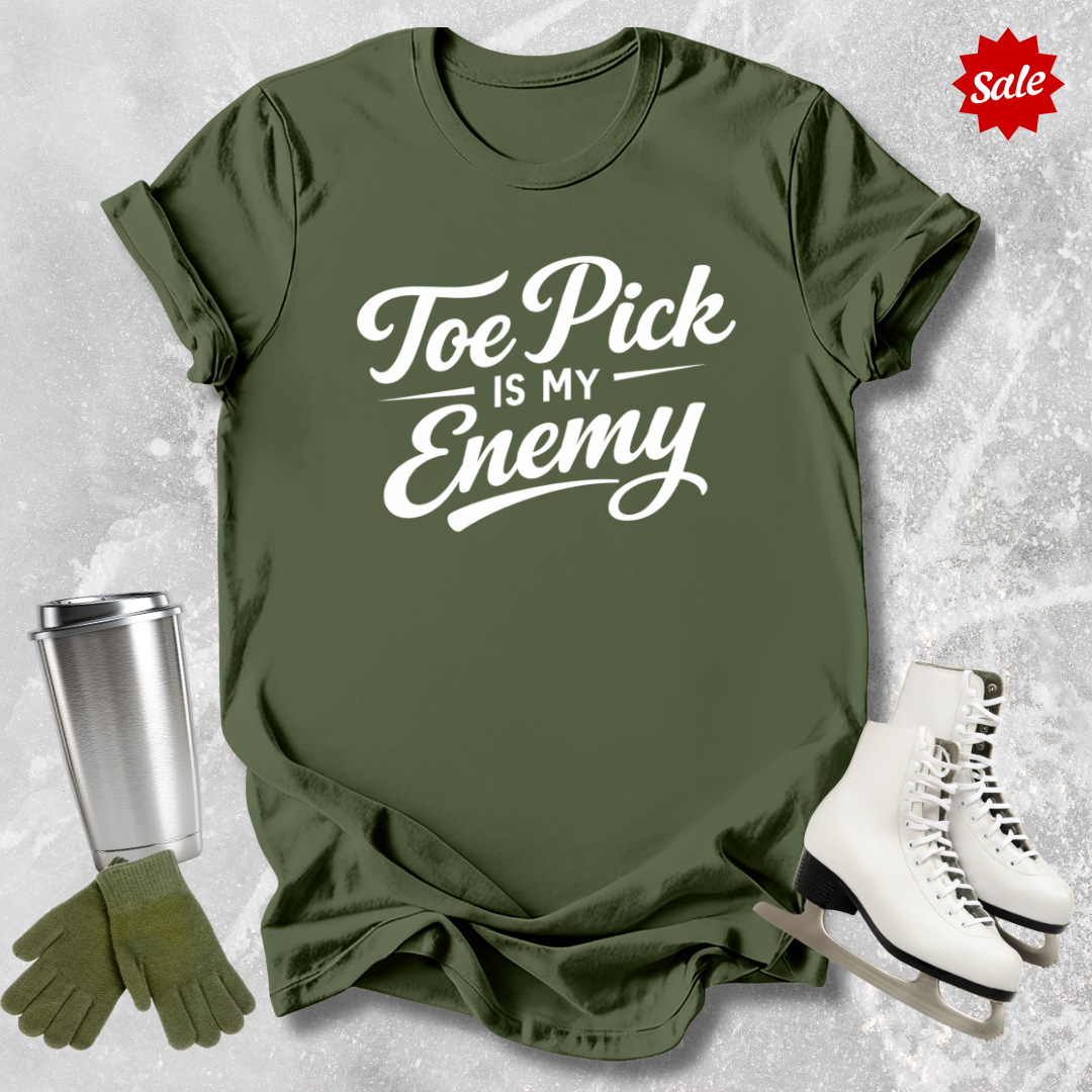 Green t-shirt with 'Toe Pick is My Enemy' text, silver tumbler, green gloves, and white skates on a textured gray background.