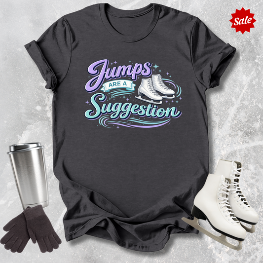 Black t-shirt with 'Jumps are a Suggestion' text, silver tumbler, black gloves, and white ice skates on a textured gray background.