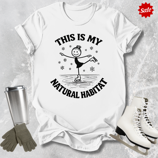 White t-shirt with 'This is my natural habitat' graphic, surrounded by ice skates, gloves, and a tumbler on a textured surface.
