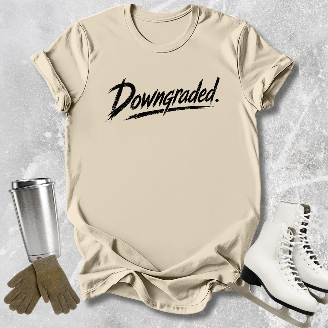 Beige t-shirt with 'Downgraded' text, silver tumbler, brown gloves, and white sneakers on a textured surface.