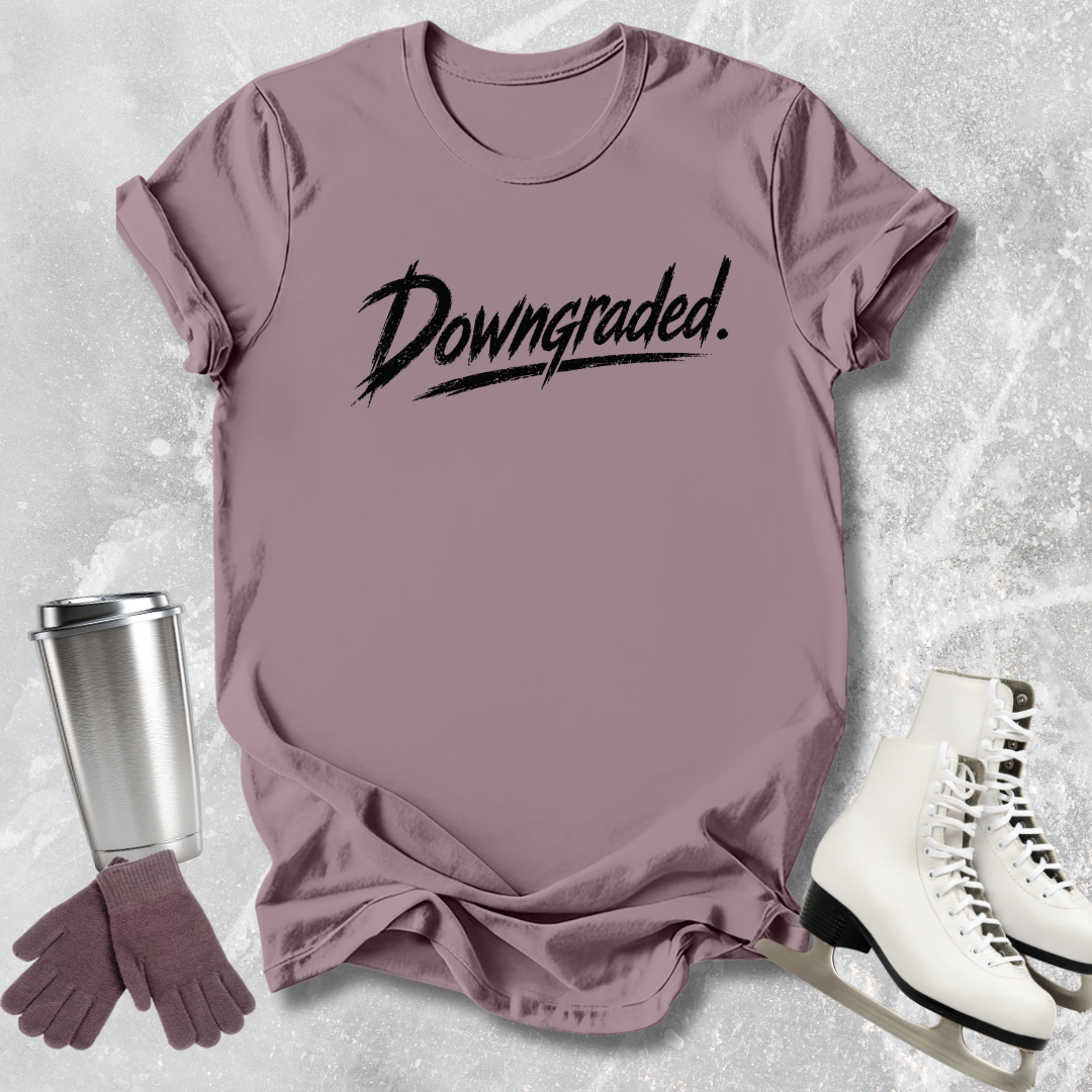 Mauve t-shirt with 'Downgraded' text, silver tumbler, purple gloves, and white skates on a textured gray background