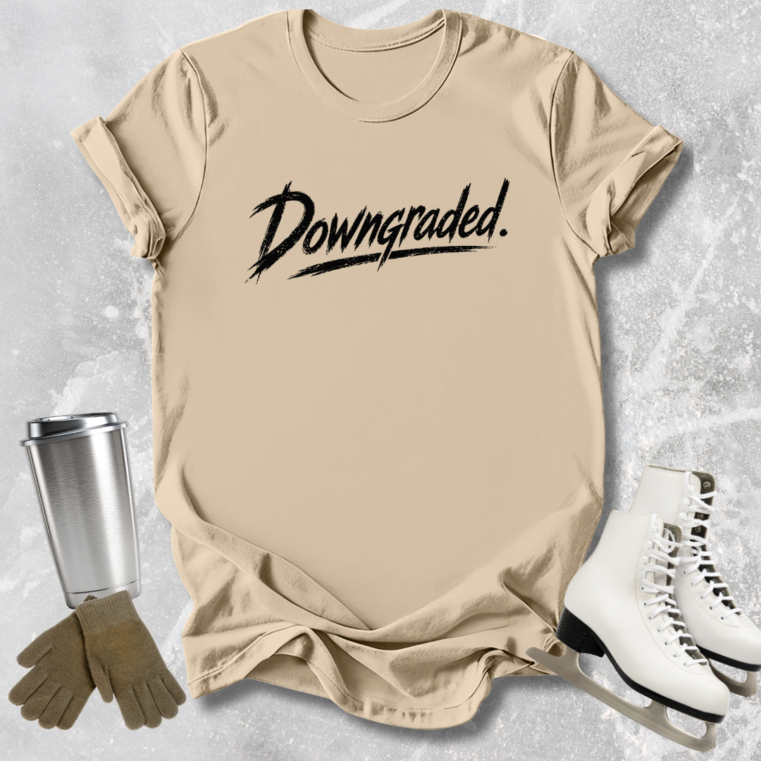 Beige t-shirt with 'Downgraded' text, silver tumbler, brown gloves, and white skates on a textured surface.
