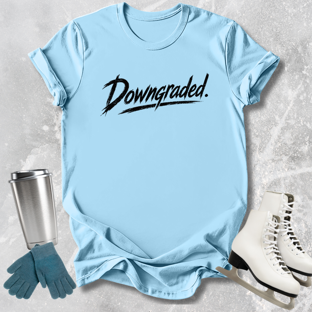 Light blue t-shirt with 'Downgraded' text, next to a silver tumbler, green gloves, and white shoes on a textured surface.