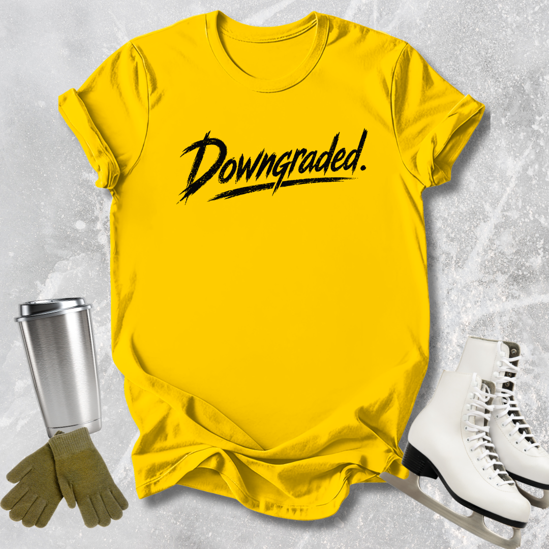 Yellow t-shirt with 'Downgraded' text, silver tumbler, green gloves, and white skates on a textured gray background