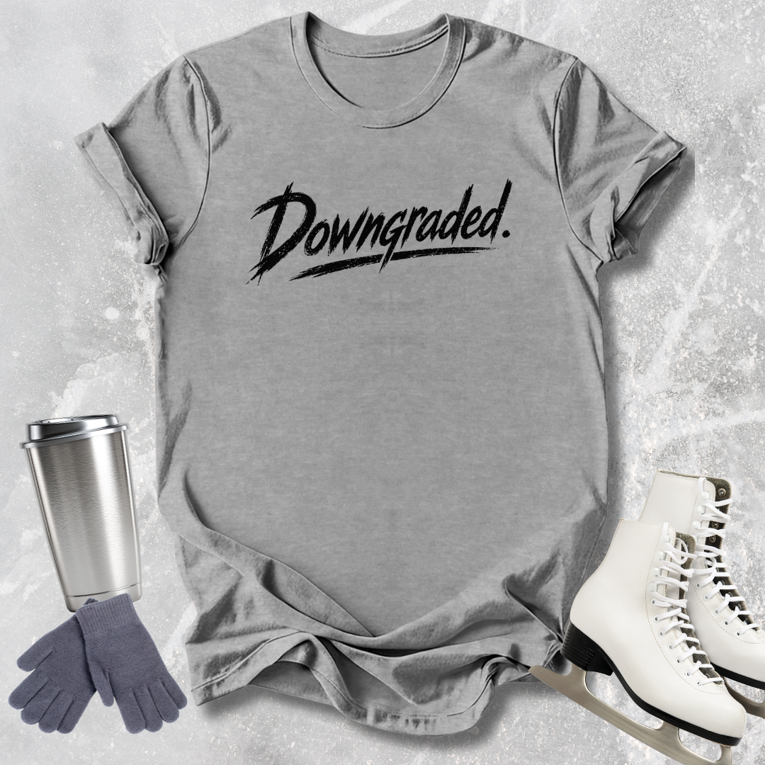 Gray t-shirt with 'Downgraded' text, silver tumbler, gray gloves, and white skates on a textured surface