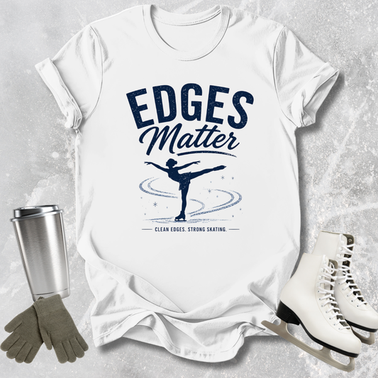 White t-shirt with 'Edges Matter' graphic on a textured surface with ice skates and gloves.