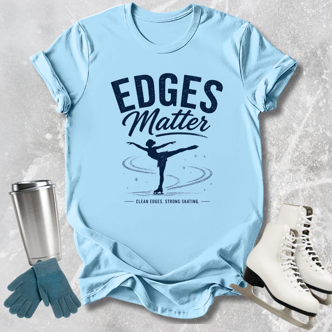 Light blue t-shirt with 'Edges Matter' graphic, next to ice skates and a tumbler on a textured surface.