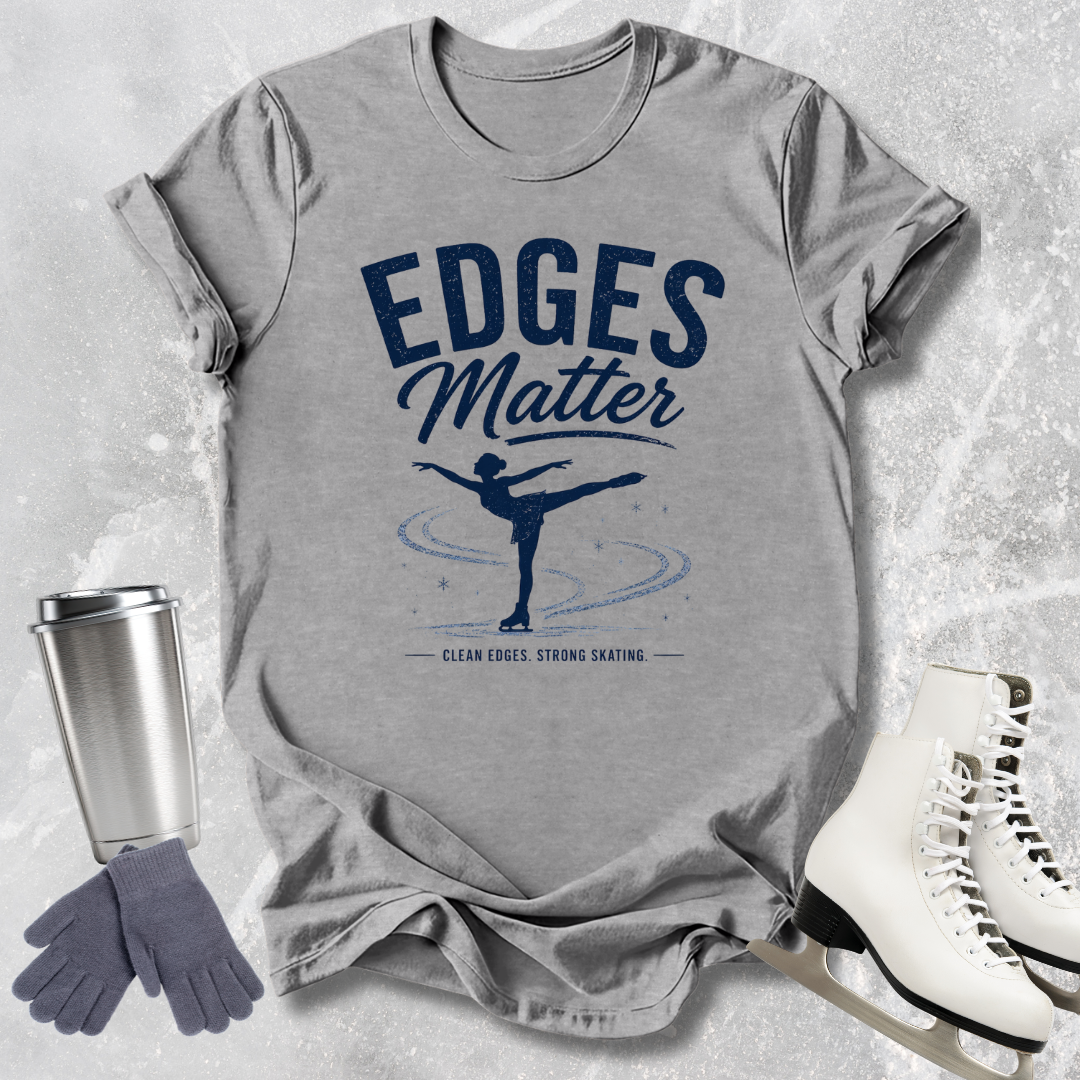 Gray t-shirt with 'Edges Matter' graphic, next to ice skates and a tumbler on a textured surface.
