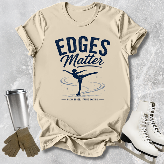 Beige t-shirt with 'Edges Matter' graphic and ice skates on a textured surface