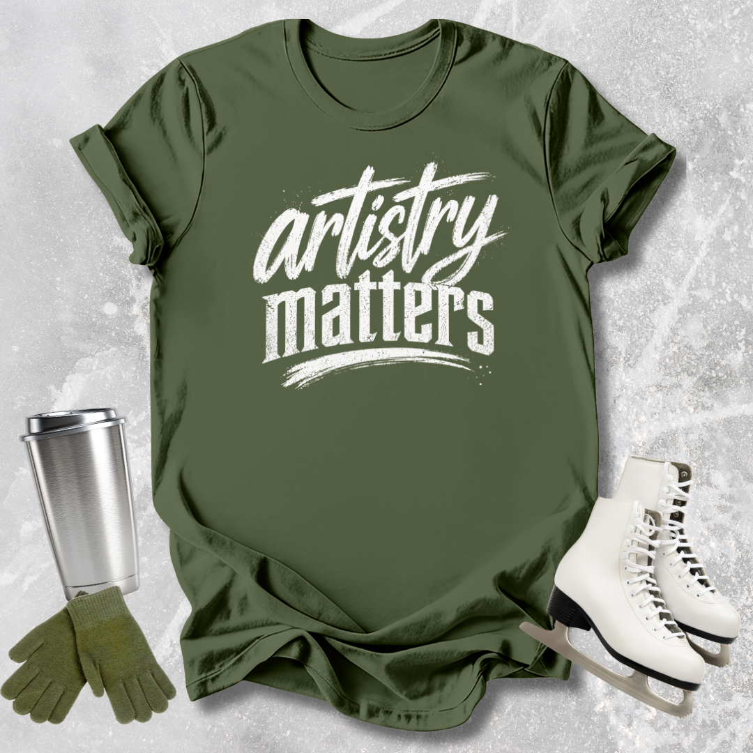 Green t-shirt with 'artistry matters' text, paired with a silver tumbler, green gloves, and white skates on a textured gray background.