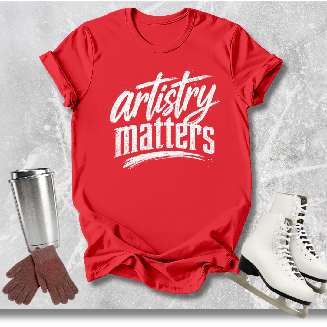 Red t-shirt with 'artistry matters' text, white skates, brown gloves, and silver cup on a textured gray background