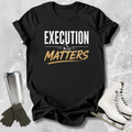 Black t-shirt with 'Execution Matters' text on a textured surface with accessories.