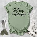 Green t-shirt with 'that was a deduction' text, next to a silver tumbler, green gloves, and white skates on a textured surface.