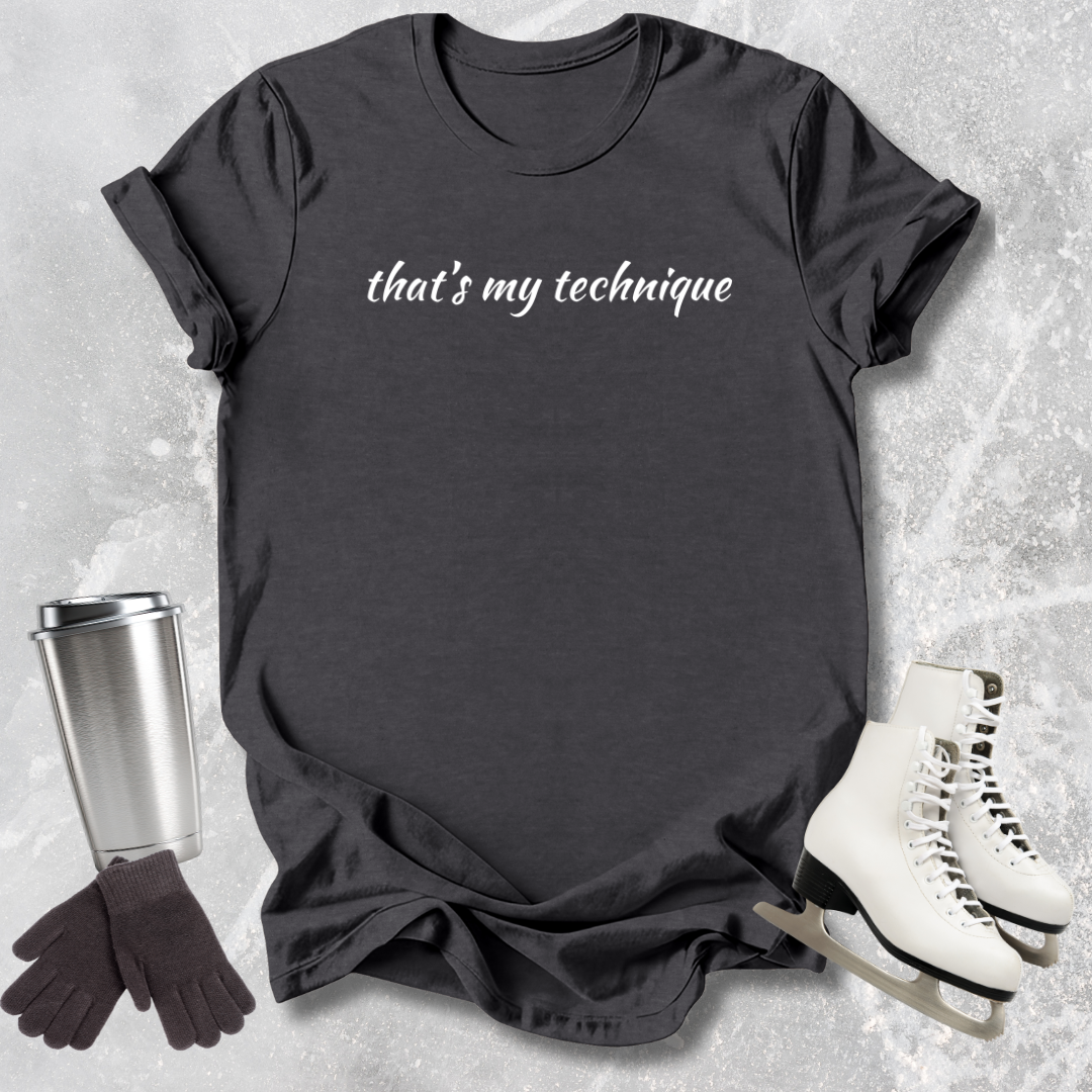 Dark gray t-shirt with 'that's my technique' text, next to a silver tumbler, black gloves, and white skates on a textured surface.