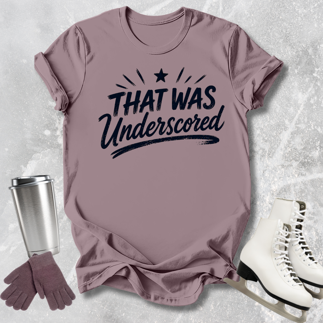 Mauve t-shirt with 'THAT WAS Underscored' text, silver tumbler, purple gloves, and white skates on a textured gray background