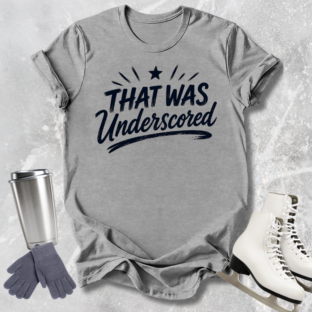 Gray t-shirt with 'That Was Underscored' text, next to a silver tumbler, gray gloves, and white skates on a textured surface.