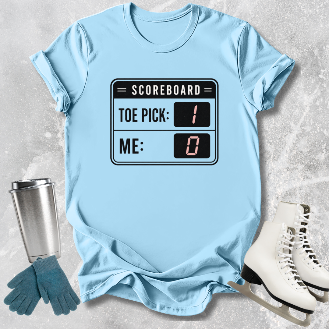 Light blue t-shirt with scoreboard design, next to a silver tumbler, green gloves, and white skates on a textured surface.