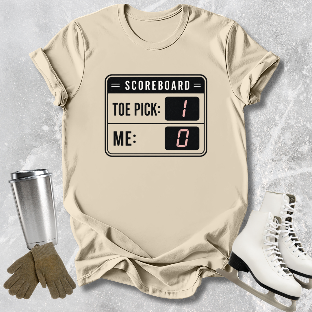 Beige t-shirt with scoreboard design, next to a silver tumbler, brown gloves, and white skates on a light gray textured background.